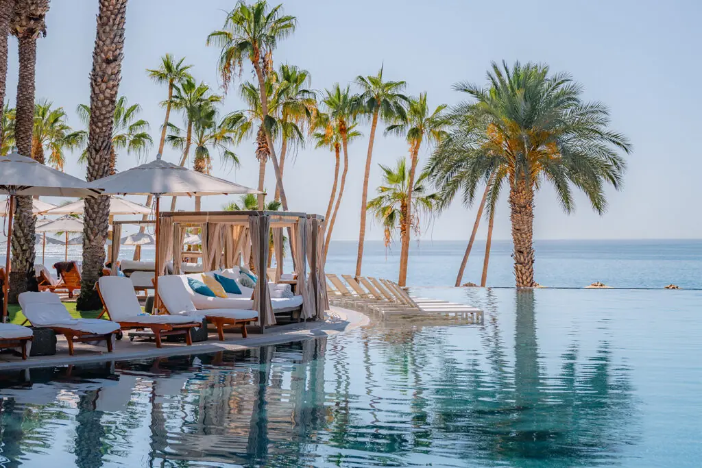 Infinity pool with cabanas and lounge chairs overlooking the ocean, surrounded by palm trees at a luxury resort.