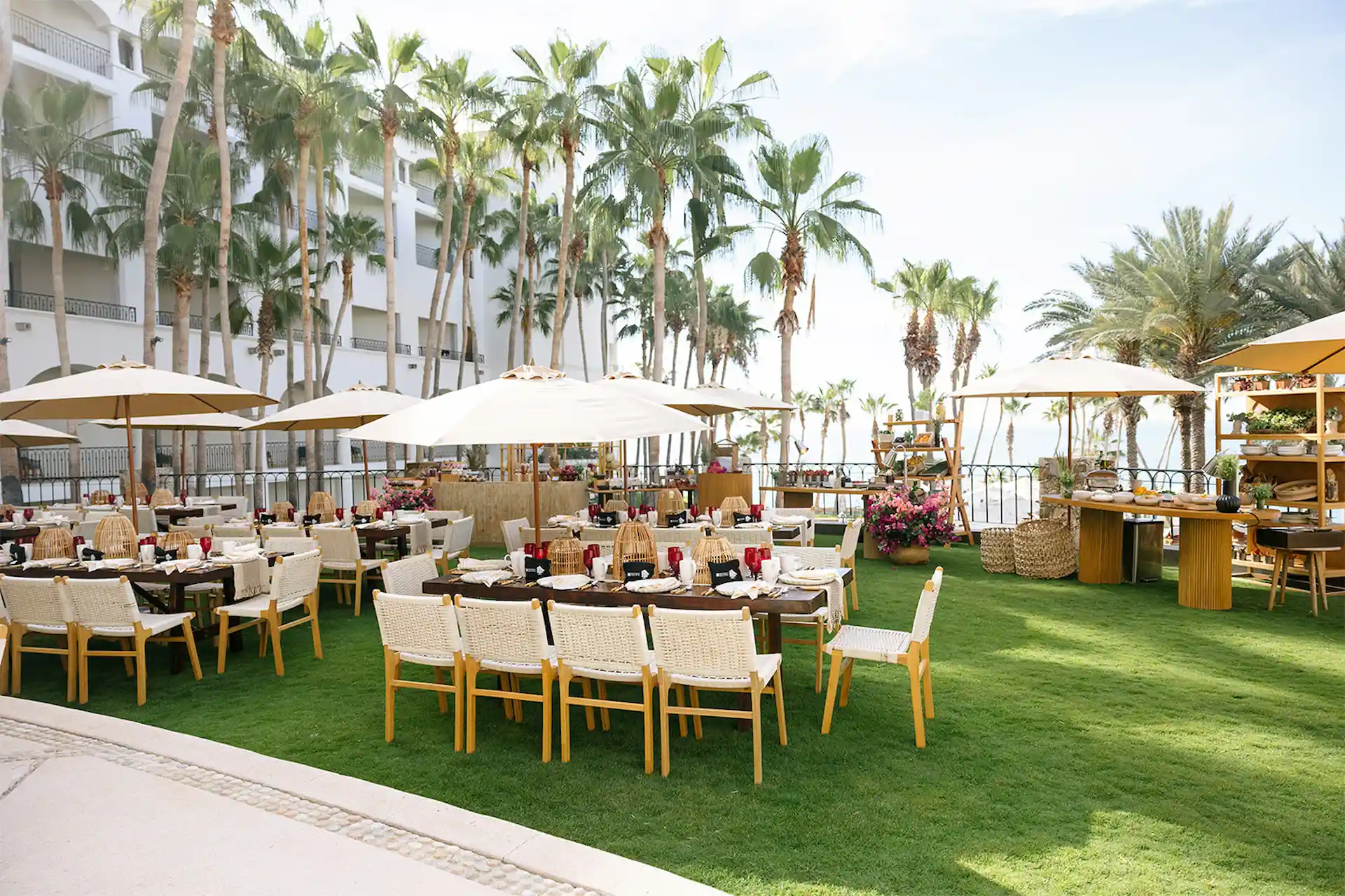 Elegant outdoor dining setup at a luxury resort, with wooden tables under beige umbrellas, red napkins and buffet stations.