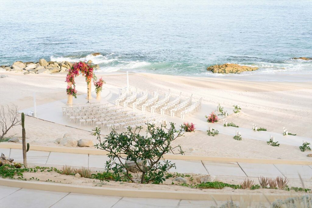 Beachfront wedding setup with white chairs and floral arch overlooking the ocean.