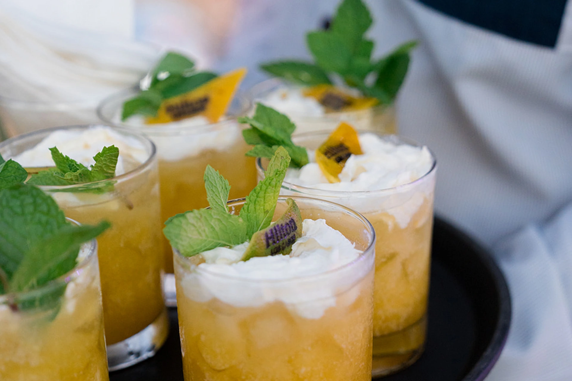 Mini vasos de postre rellenos de puré de mango, cubiertos con crema batida, hojas de menta fresca y rodajas de kiwi.