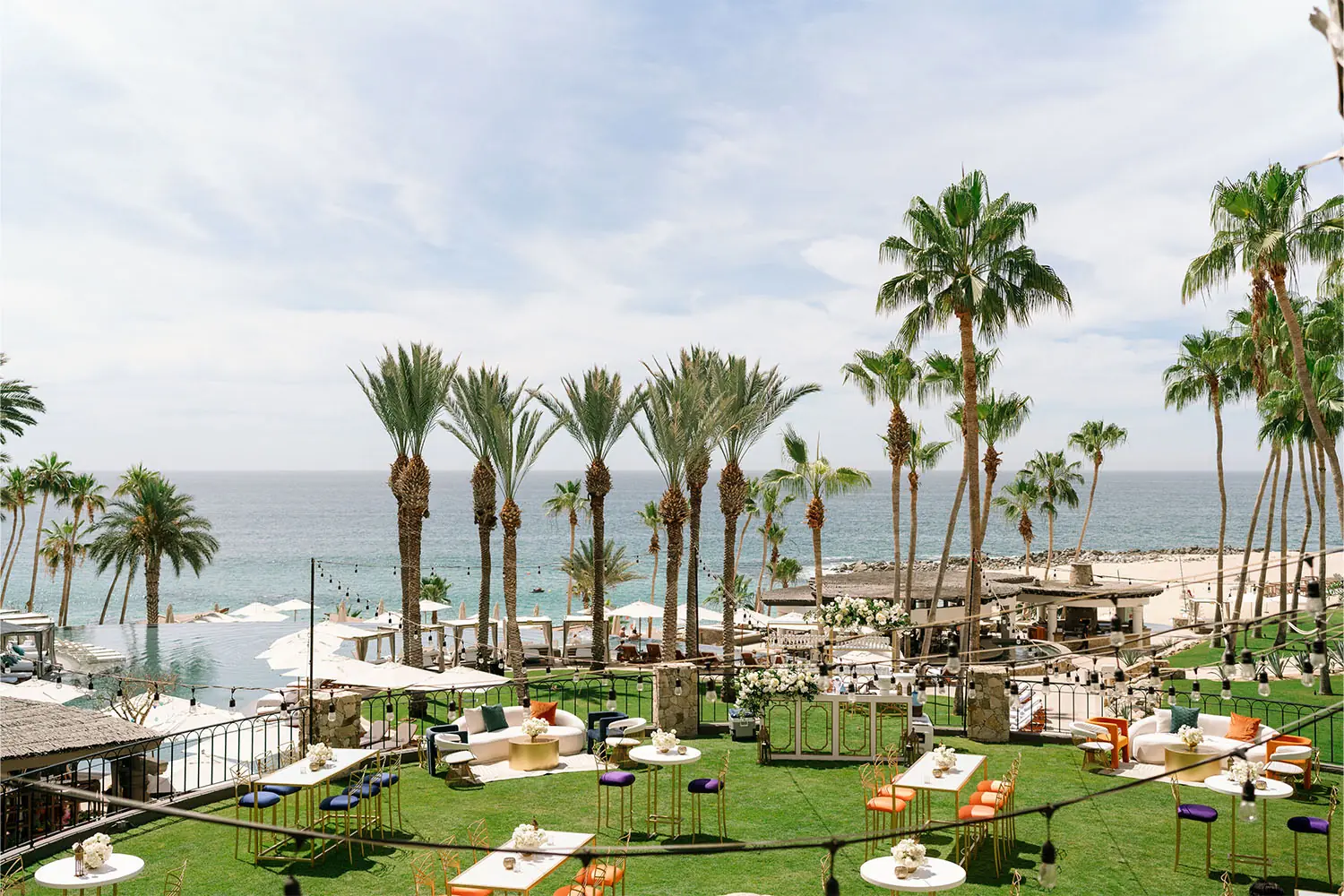 Montaje para eventos al aire libre frente al mar con palmeras, asientos tipo lounge y mesas con vista al mar.