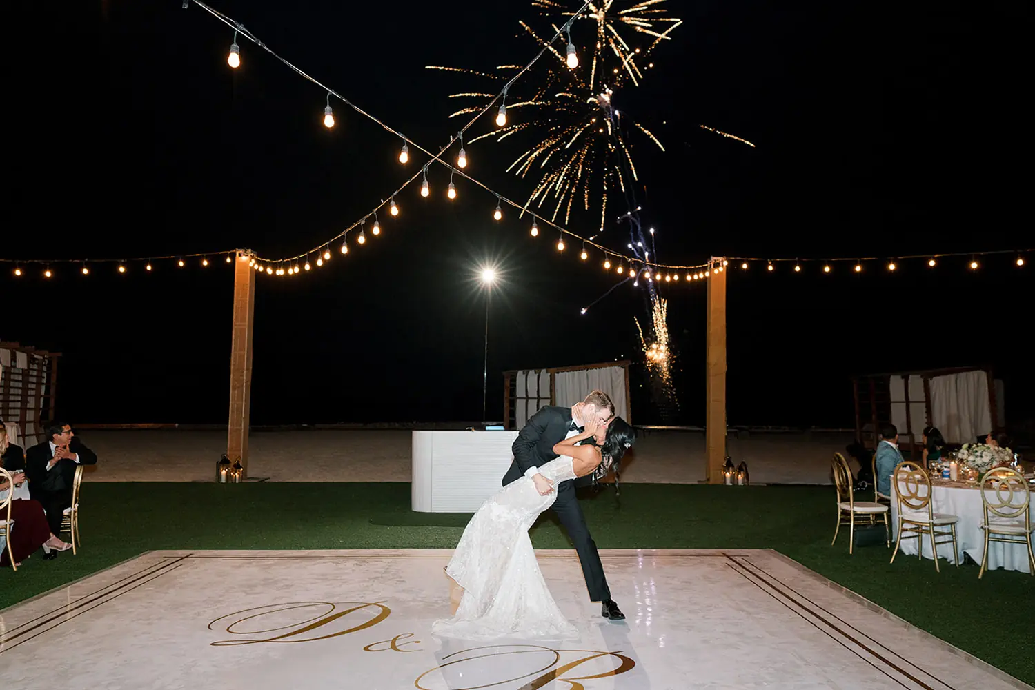 Los novios comparten el primer baile bajo luces de colores y fuegos artificiales durante una recepción de boda al aire libre por la noche.