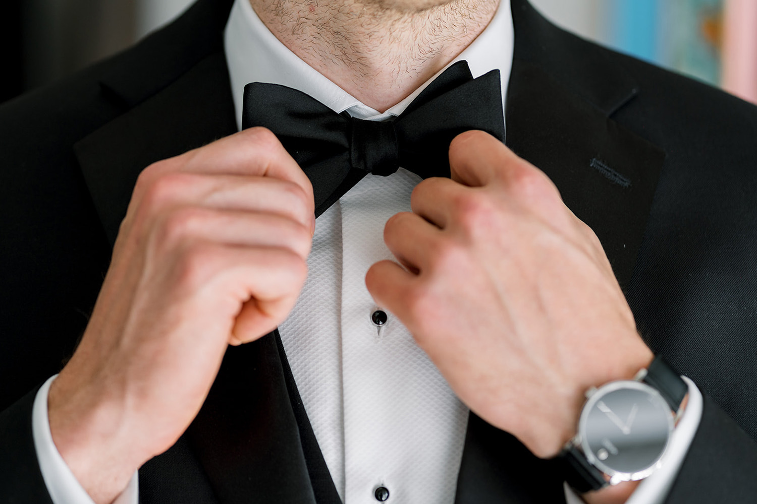 Primer plano de un hombre ajustándose una pajarita negra mientras viste un esmoquin.