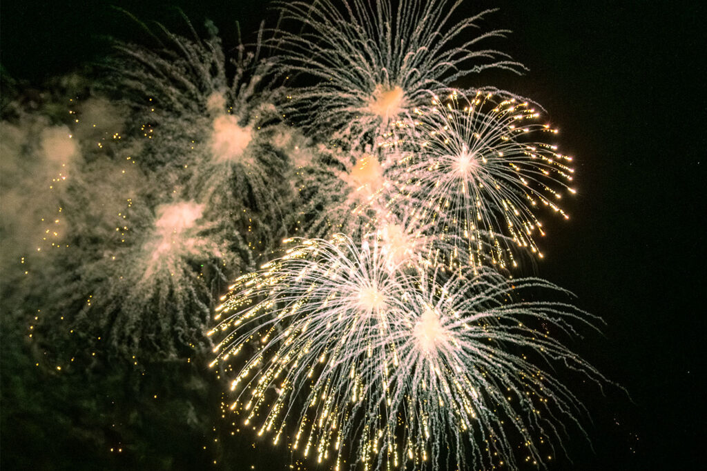 Bright white and gold fireworks bursting in the night sky during a celebration.