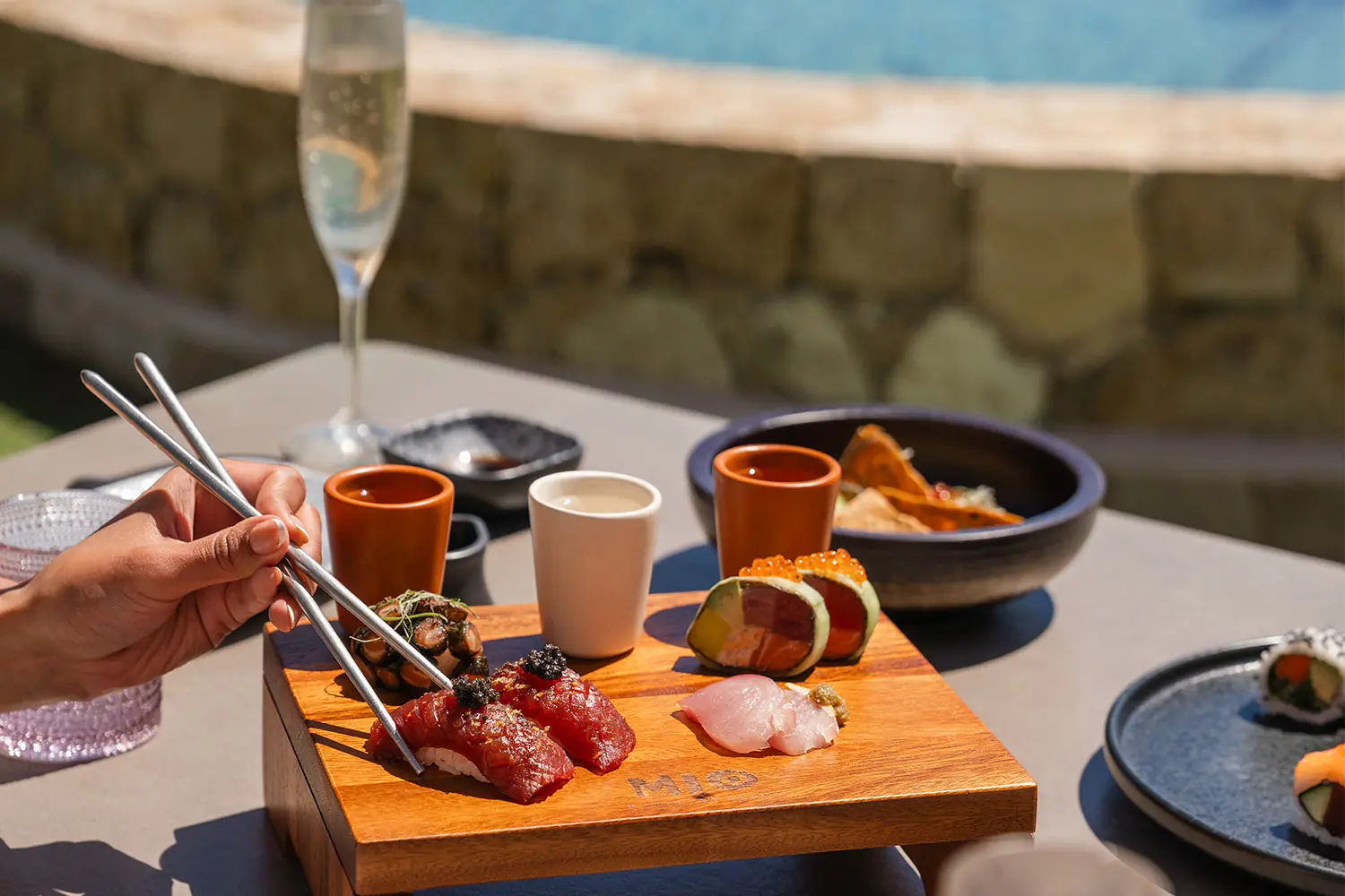 A hand uses chopsticks to enjoy a fresh sashimi plate paired with champagne at Mio restaurant at Hilton Los Cabos Beach & Golf Resort