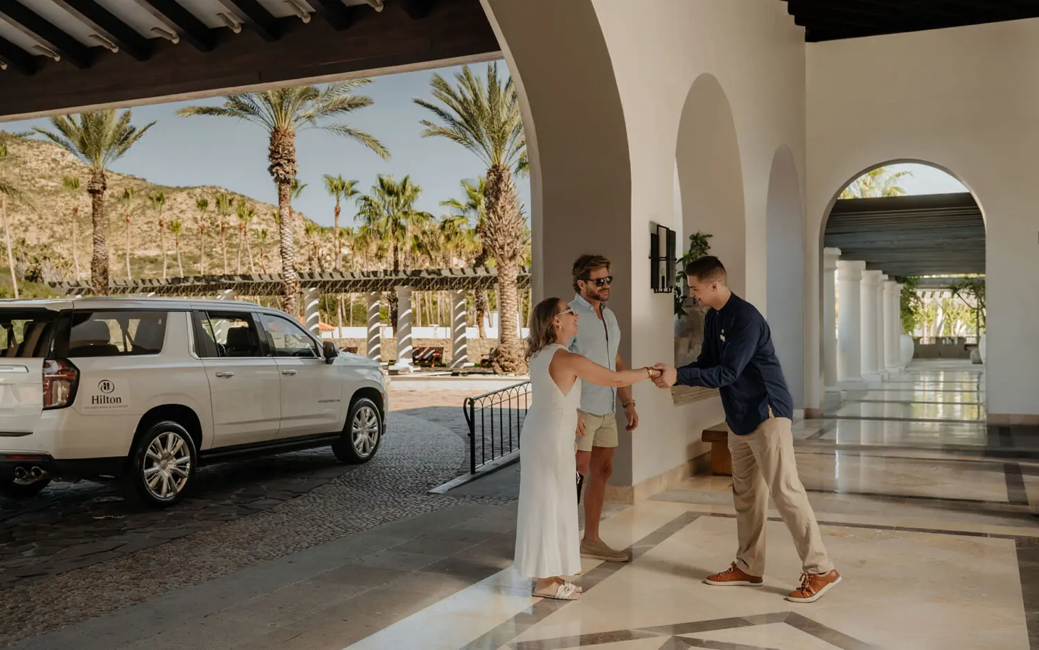 A Compadre Concierge team member greets arriving guests at the entrance of Hilton Los Cabos Beach & Golf Resort