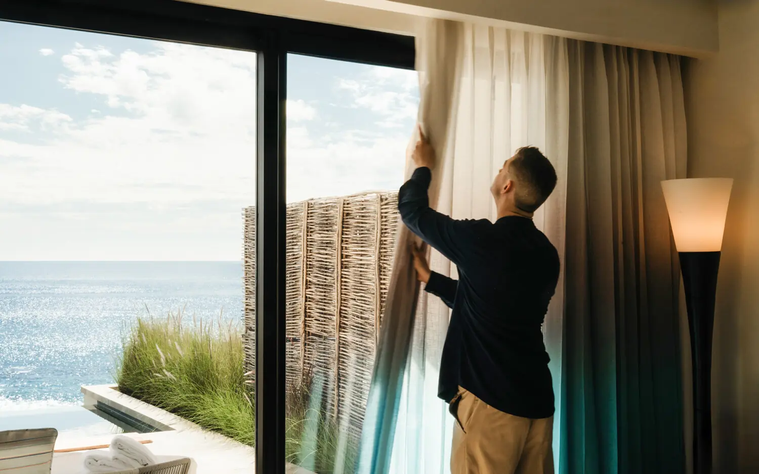 Un miembro del equipo de conserjería de Compadre abre las cortinas para revelar una suite con vista al mar en el Hilton Los Cabos Beach & Golf Resort.